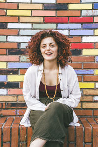 Portrait of woman sitting by colorful brick wall