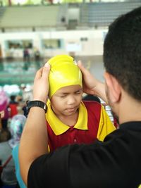 Man helping boy put on swimming cap