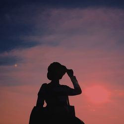 Silhouette woman in hat standing against orange sky