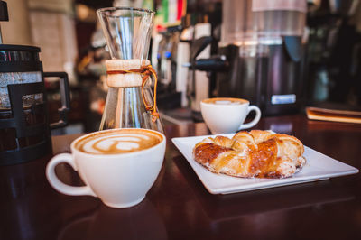 Close-up of cappuccinos and croissant served on table