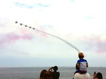 People walking airplanes with trails in flight