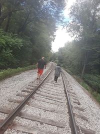 Rear view of people walking on railroad track in forest