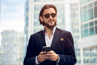 Smiling businessman using mobile phone while standing outdoors