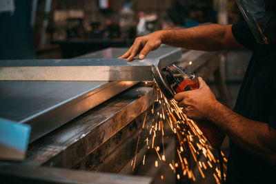 Unrecognizable person working in a workshop cutting metal, sparks are seen