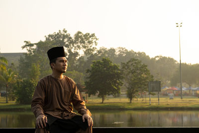 Man wearing traditional clothing while sitting against lake during sunset