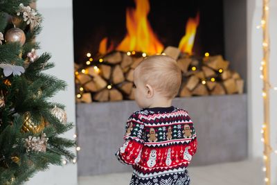Rear view of boy standing by christmas tree at home