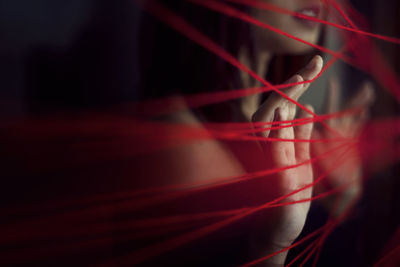 Midsection of woman touching red strings in darkroom