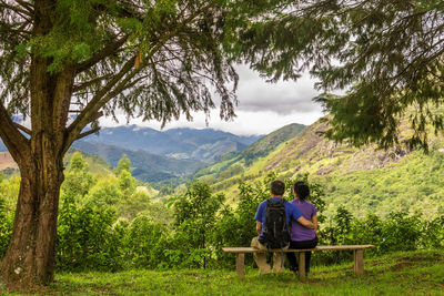 Rear view of couple looking at mountains while sitting on bench 