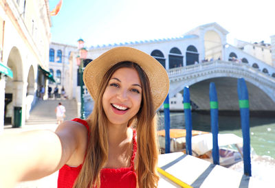 Portrait of smiling young woman standing against built structure