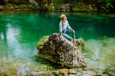 Young woman sitting on rock by lake