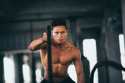 Shirtless young man exercising with rope at gym