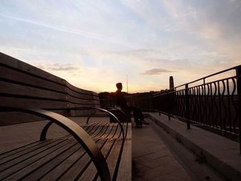 Man sitting on bench at observation point against sky during sunset
