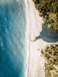 Aerial top down view of beach with blue sea and small river mouth enclosed by green trees