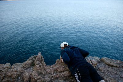 Rear view of man sitting on rock by sea