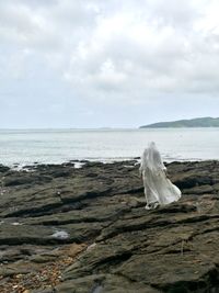 Rear view of woman walking on rocks at beach against sky