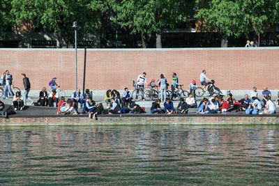 People relaxing at riverbank against wall