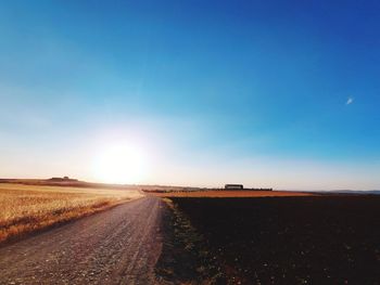 Road amidst field against sky during sunset