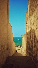 Scenic view of alley leading to sea against clear sky