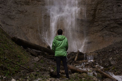 Rear view of man standing on rock looking at waterfall