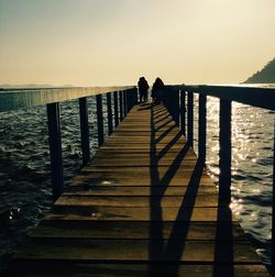 Silhouette people on pier at sea against clear sky