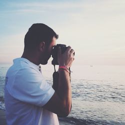 Side view of young man standing at beach against sky