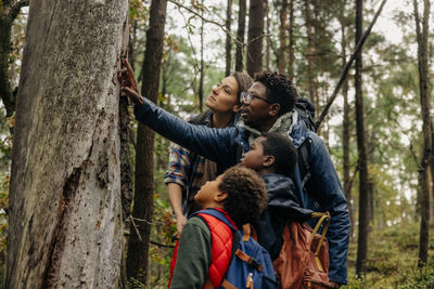 Father showing tree while talking with family during vacation in forest