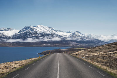 Road by snowcapped mountains against clear sky