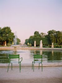 Empty chairs by swimming pool against clear sky