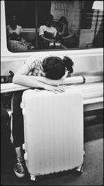 Tired woman leaning on wheeled luggage in train