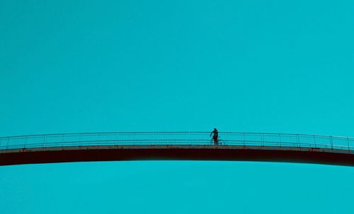 Man standing on bridge against clear blue sky