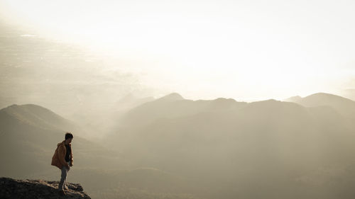 Rear view of man standing on mountain against sky during sunset