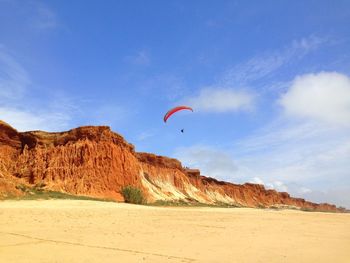 Low angle view of paraglider over rock formation at praia da falesia against sky