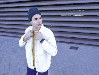 High angle of elegant man in street clothes and green hat looking away while adjusting jacket