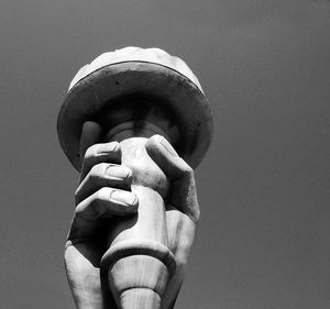 Low angle view of hand holding sculpture against sky