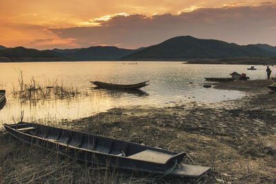 Boat moored on lake against sky during sunset