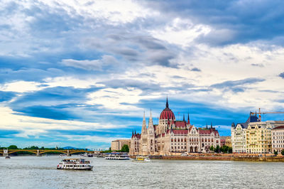 View of building by river against cloudy sky