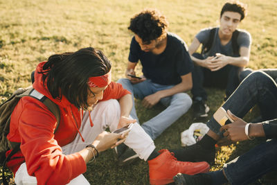 High angle view of friends using mobile phones while sitting on field