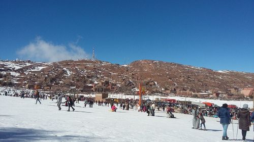 Group of people on snowy mountain against blue sky