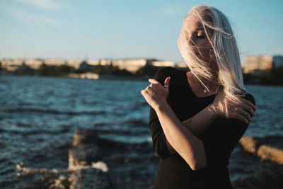 Woman with tousled hair standing against sea during sunset