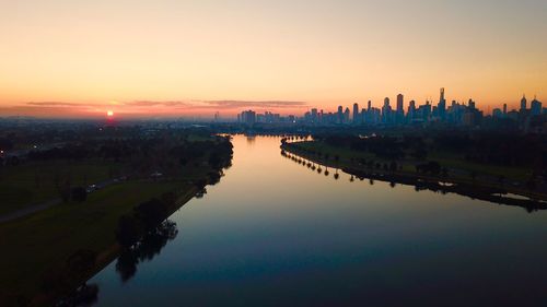Scenic view of river by buildings against sky during sunset