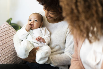 Aunt holding niece while mother sitting beside at home