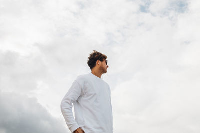 Side view of young man looking away against sky