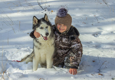 Portrait of smiling boy with dog sitting on snow covered land