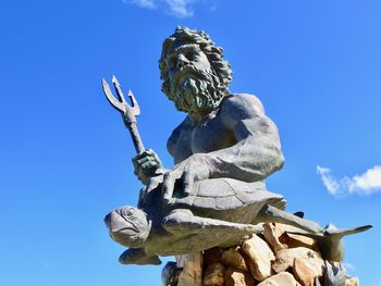 Low angle view of poseidon statue against blue sky