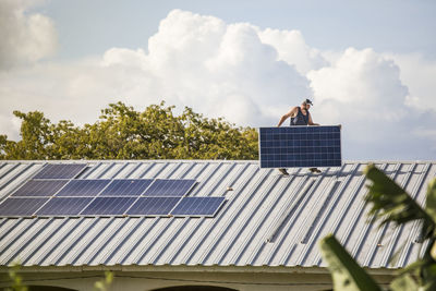 Construction worker carries solar panel across roof during install.