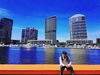 Man sitting on retaining wall against lake in city