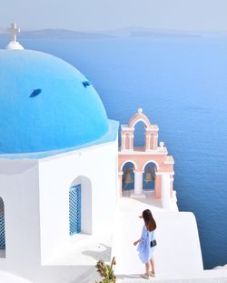 People in front of building by sea against blue sky