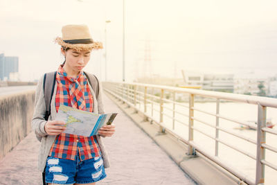 Woman reading map while standing in city against sky