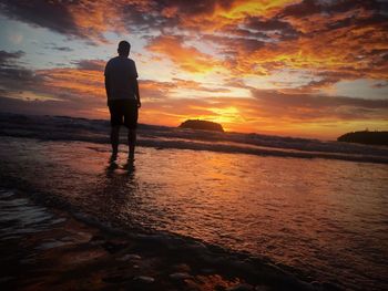 Silhouette man standing on beach against sky during sunset