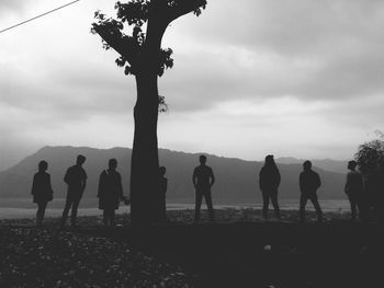 Silhouette people standing by tree against sky